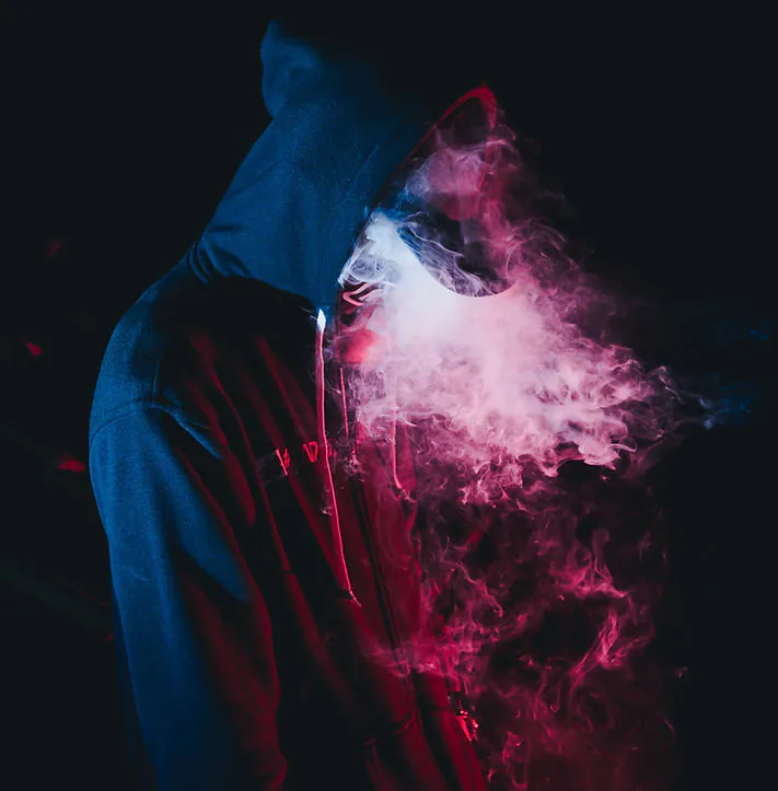 Man in a hoodie exhaling vape smoke